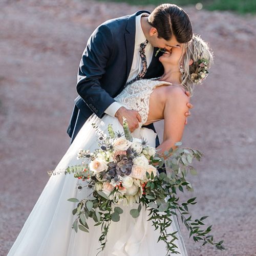 groom kissing bride holding wedding flowers