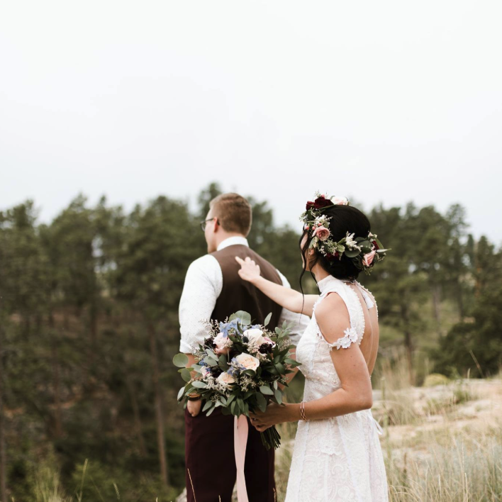 Bride behind her husband tapping him on the shoulder holding her wedding bouquet and flower crown