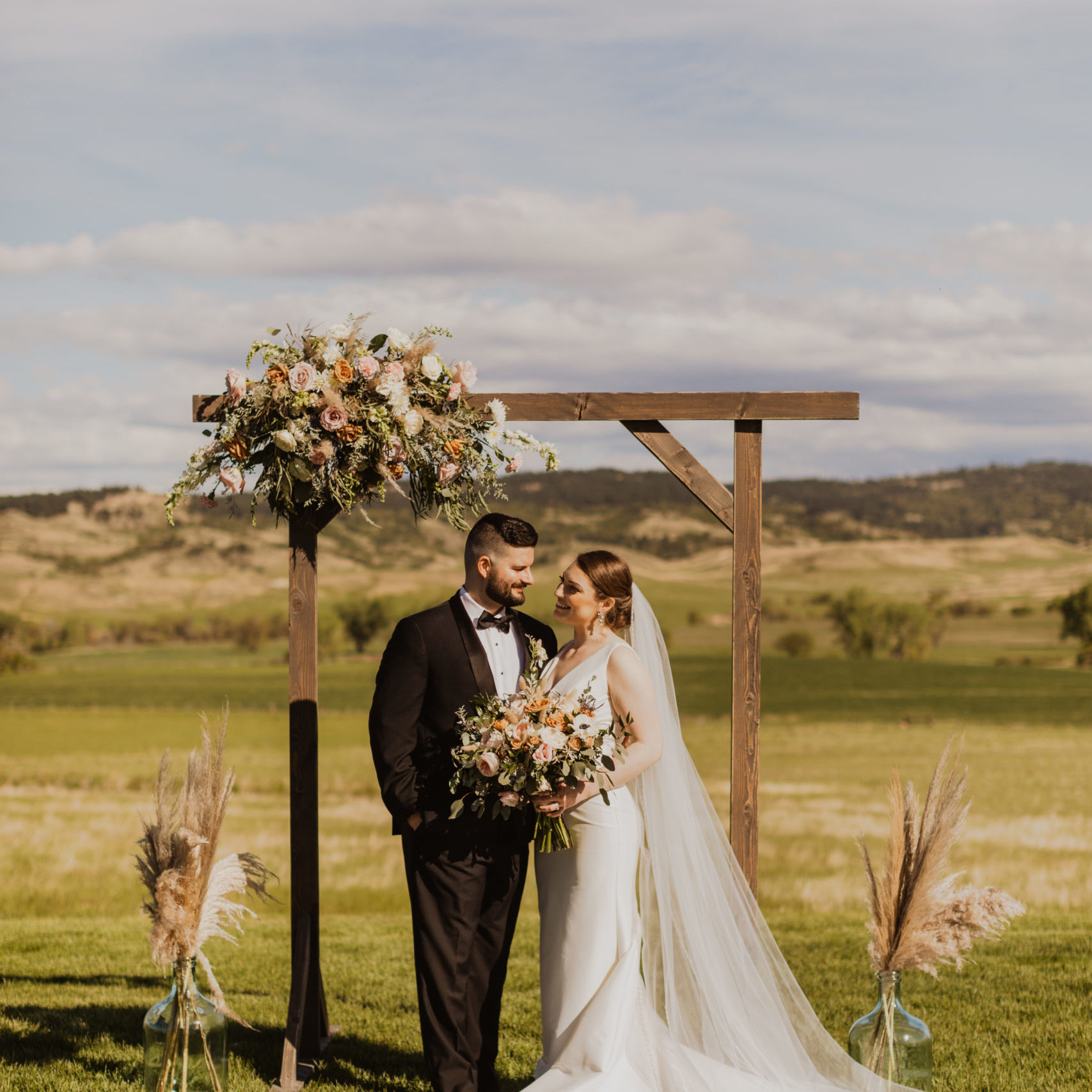 Bride and groom standing before flower arrangement and holding bouquet